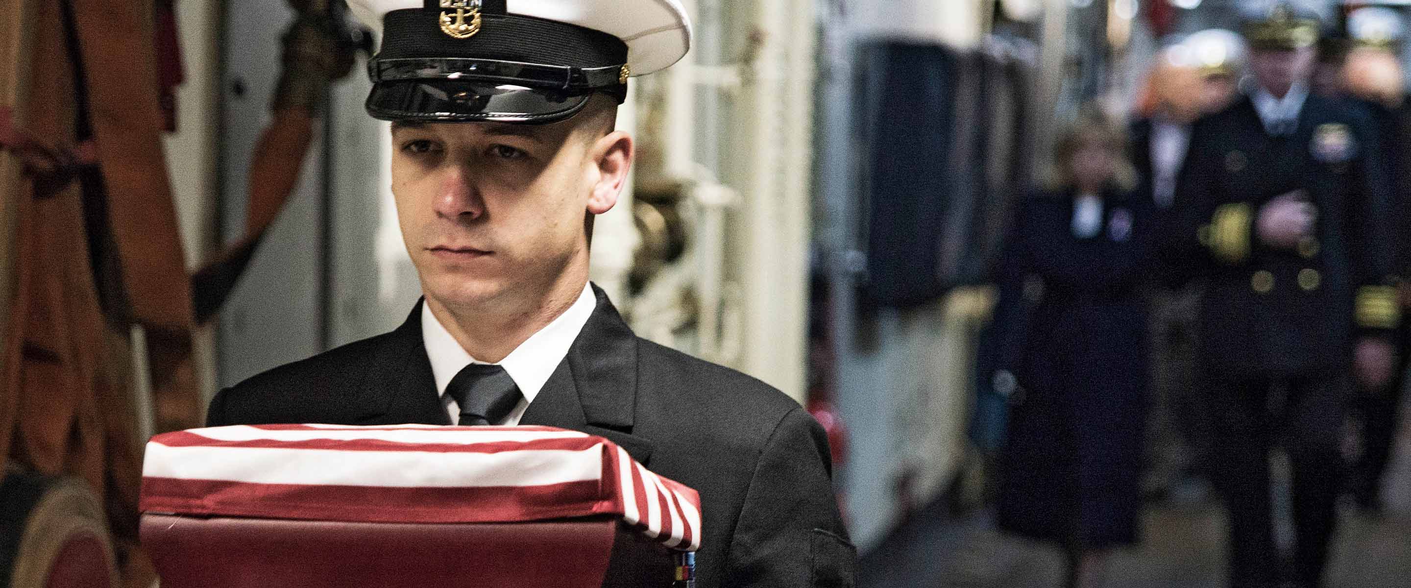 Navy religious programming specialist carries a folded American Flag