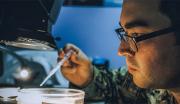 A United States Navy Sailor uses a high-powered microscope to analyze a test sample while working in a laboratory aboard a ship.