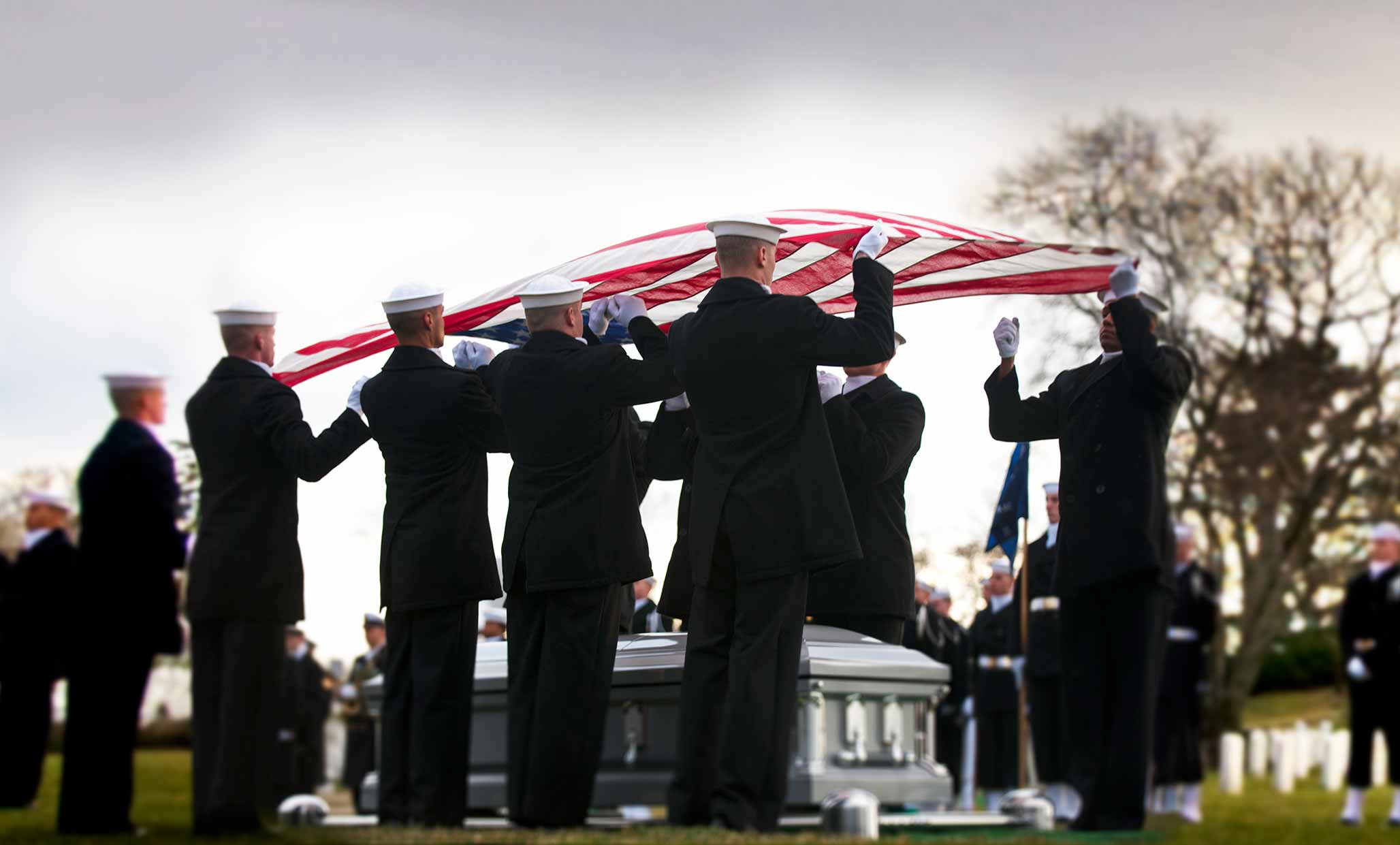 Navy members drape the American flag over a casket during a funeral ceremony for a fallen comrade