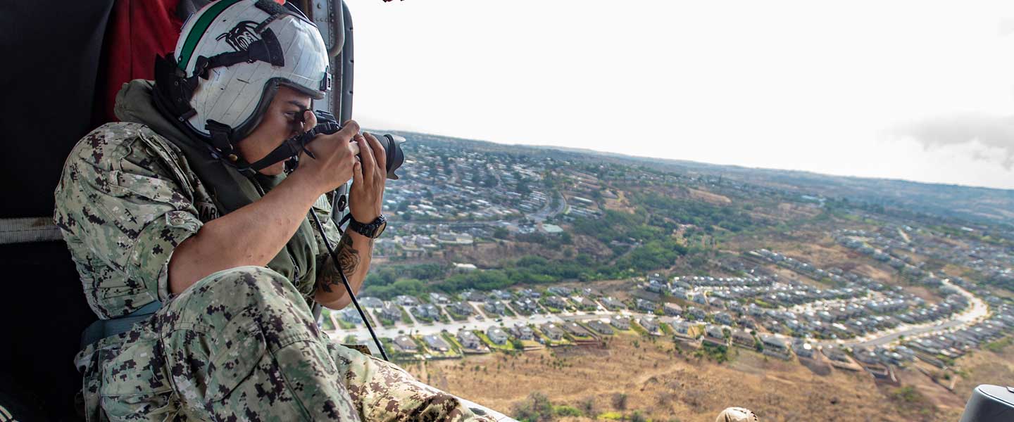 A Navy photographer takes aerial photos from a Navy helicopter