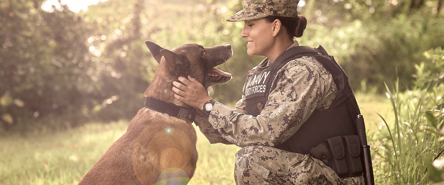 Master-at-Arms Rachel Higuera pets and smiles at her Military Working Dog, Chucky, a large Belgian Malinois