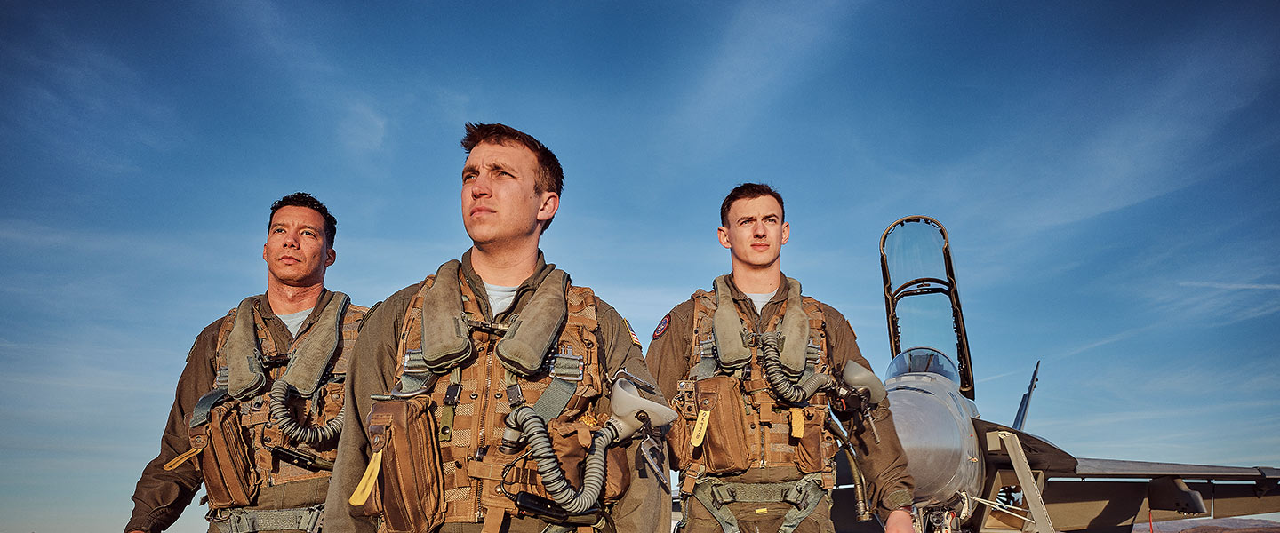 Real TOPGUN Navy fighter pilots walk across the flight deck to an F/A-18 Super Hornet fighter jet