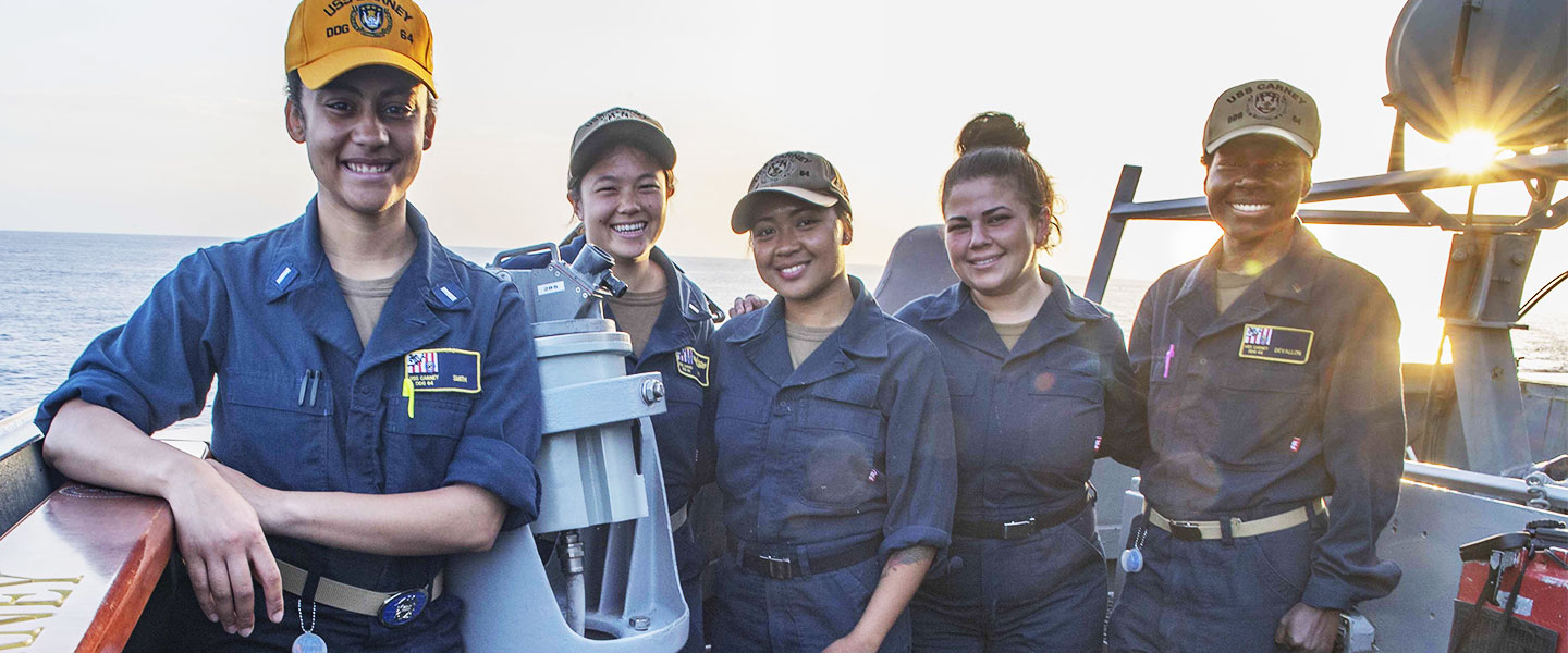Diverse women U.S. Navy Sailors pose for a photo aboard a Navy ship while out to sea