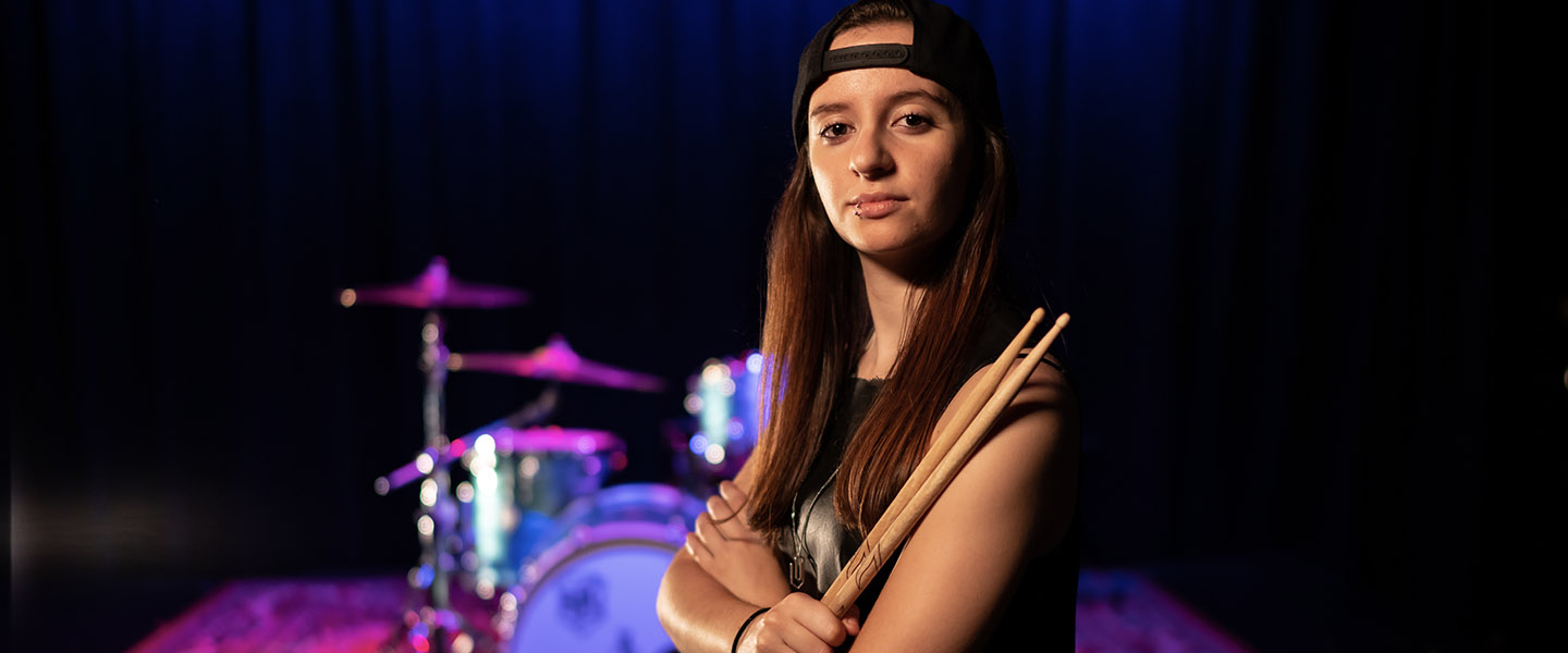 YouTube Creator Kristina Schiano stands with her drum sticks in from of her drum set.