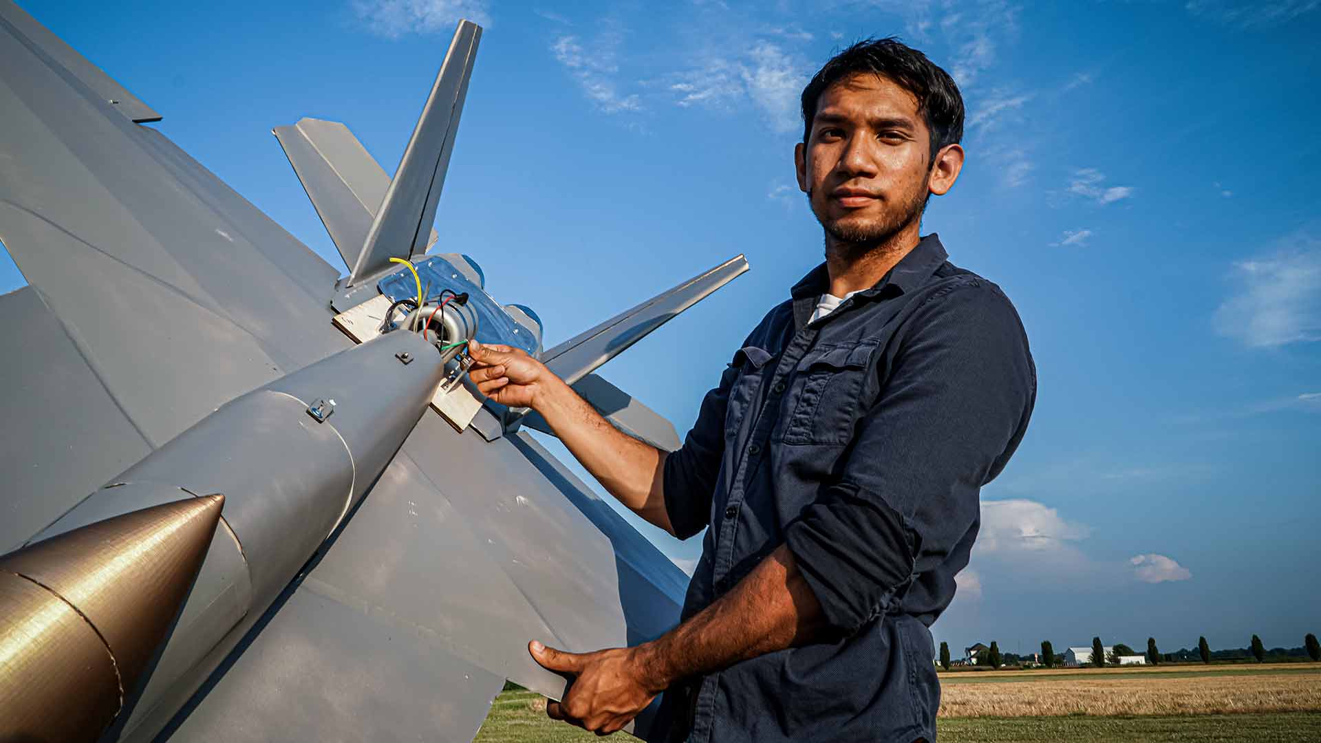 YouTube Creator Peter Stripol stands in an open field holding his large model F-18 as part of the US Navy's sailor vs. series.