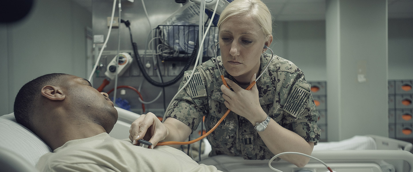 US female navy nurse examines a sailors heart rate in an onboard an aircraft carrier hospital room