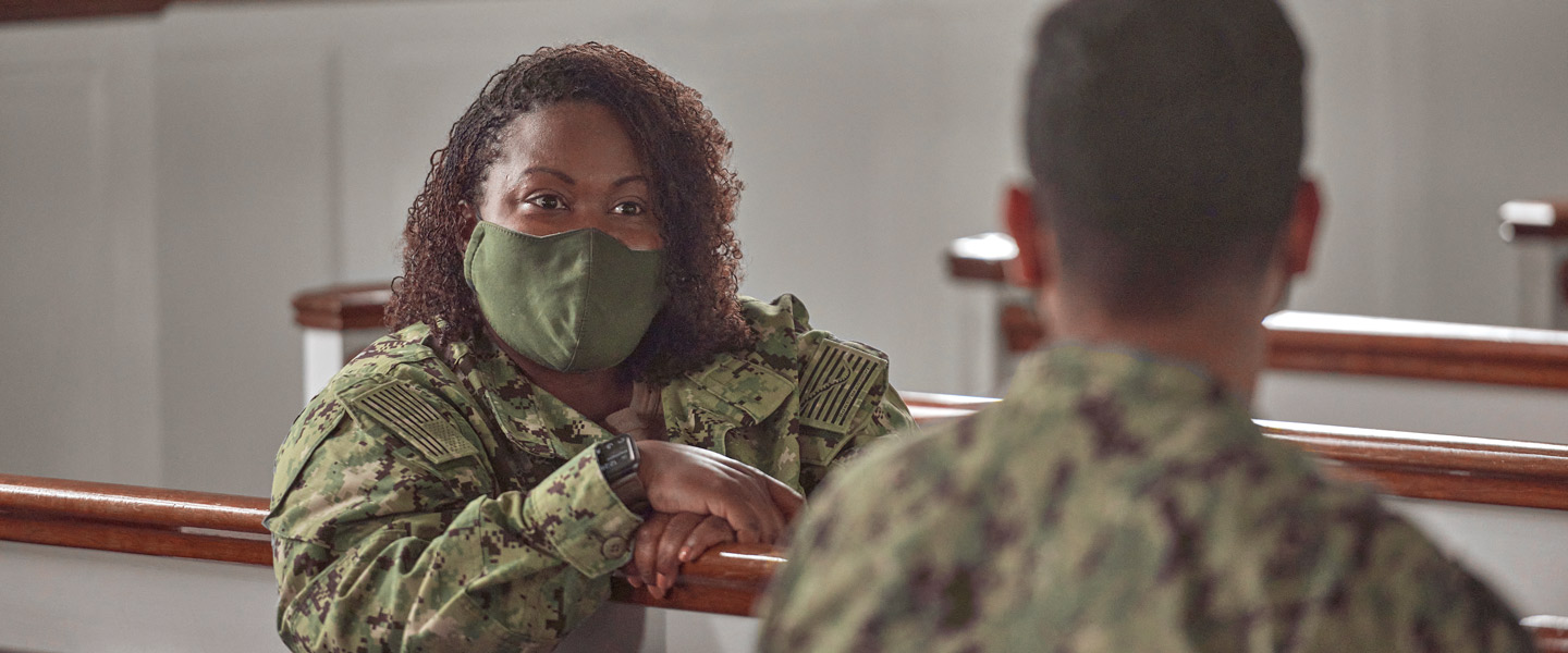 Navy chaplain Autumn Wilson sits in a chapel pew wearing Navy fatigues counseling a fellow Navy sailor