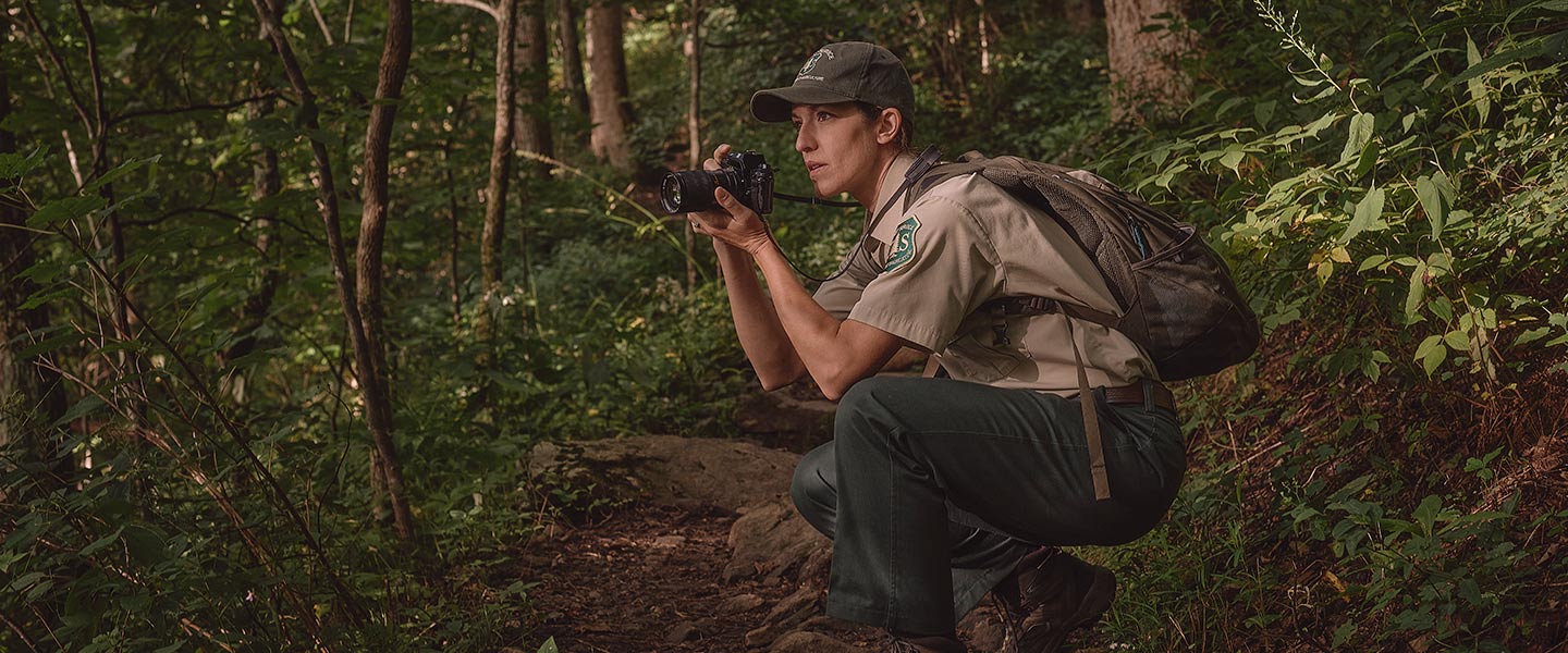 Navy mass communications specialist Kathleen Golby crouches in the middle of a forest to take photos in her role with the Park Service. 