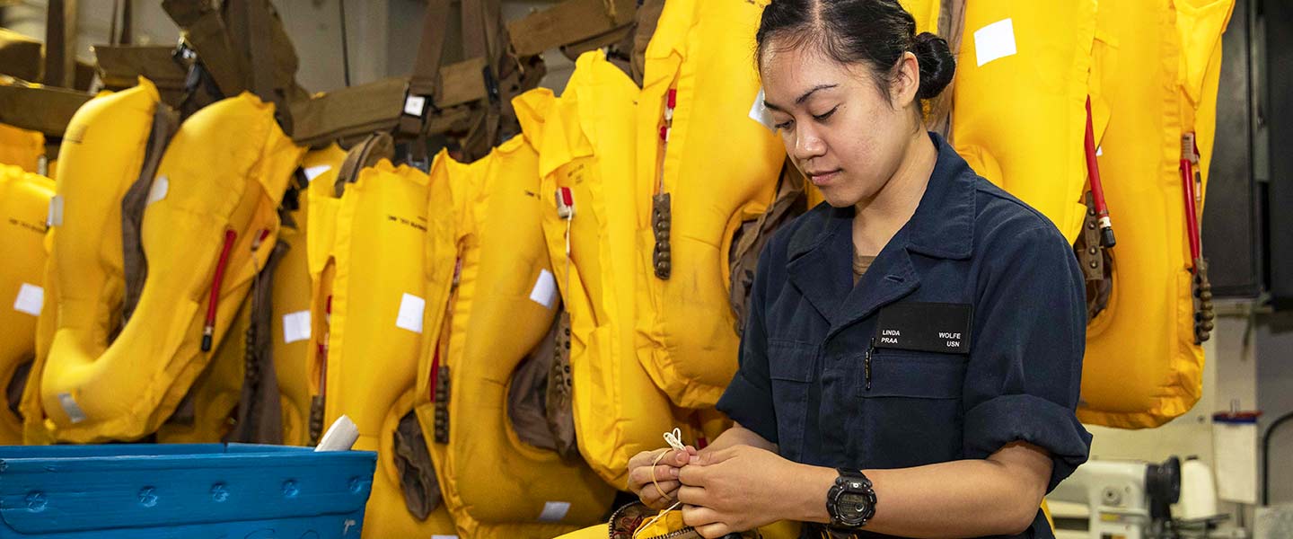 A United States Aircrew Survival Equipmentman stows a chem light in the survival pouch of a life preserver unit in the aviation survival equipment shop aboard the USS Kearsarge.