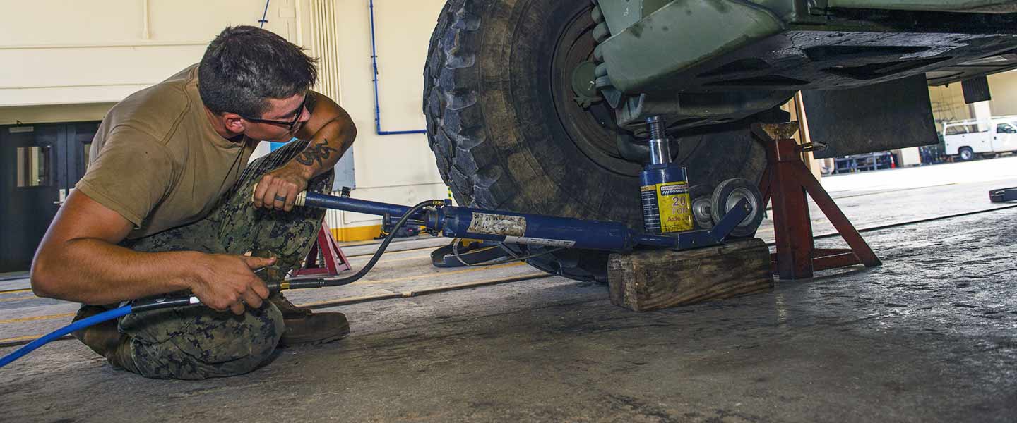 A United States Navy Construction Mechanic positions a jack before conducting a vehicle safety inspection.