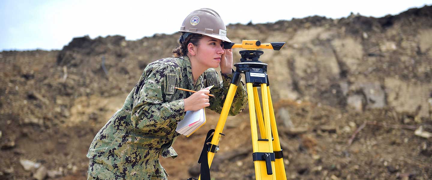 A United States Engineering Aide checks the elevation of a construction site with a level.