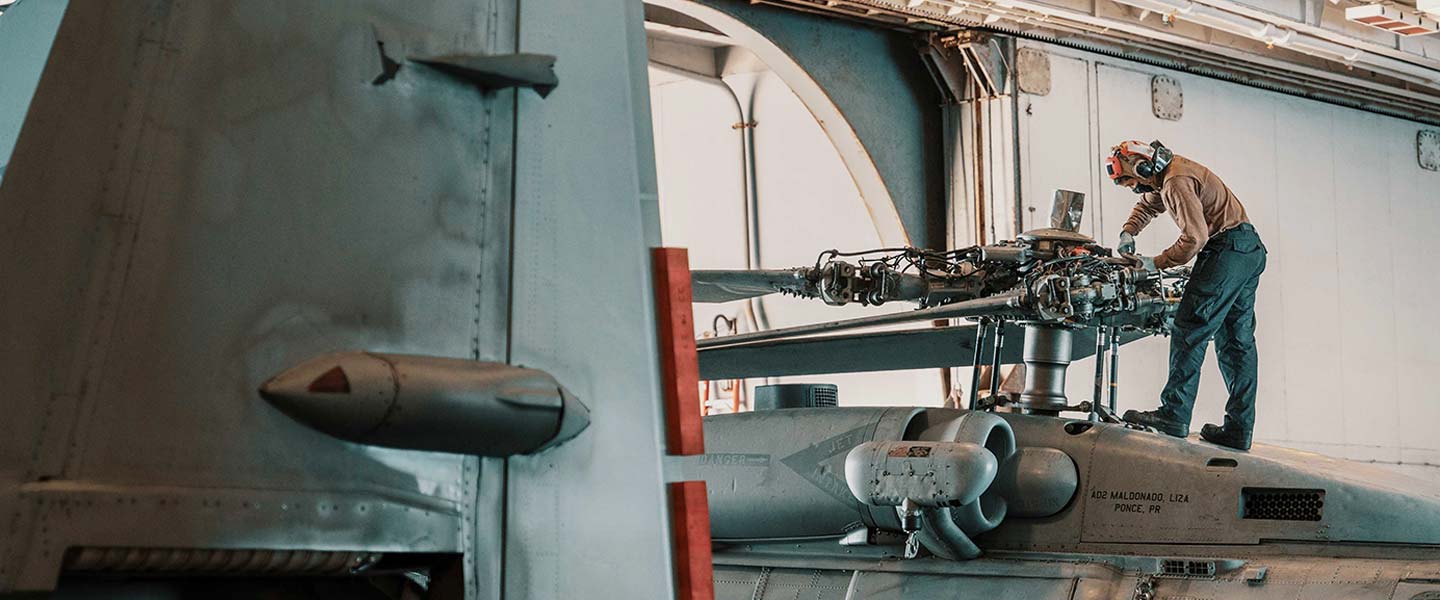 A United States Navy Aviation Structural Mechanic conducts maintenance on an MH-60R Sea Hawk in the hangar bay of the aircraft carrier USS Theodore Roosevelt.