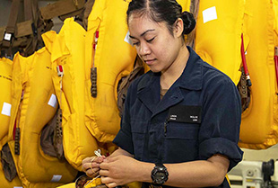 A United States Aircrew Survival Equipmentman stows a chem light in the survival pouch of a life preserver unit in the aviation survival equipment shop aboard the USS Kearsarge.