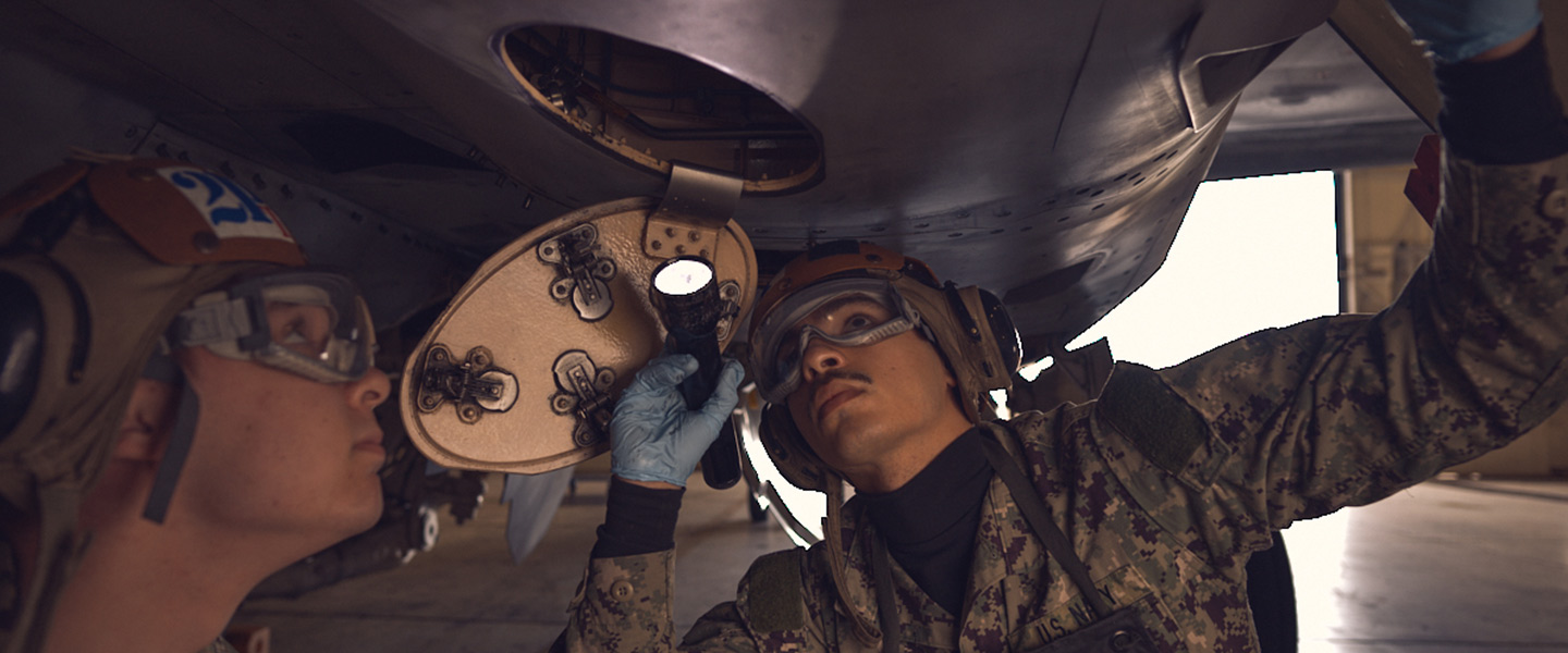 United States Navy Aviation Electronics Technicians perform equipment repairs on an aircraft in a hangar.