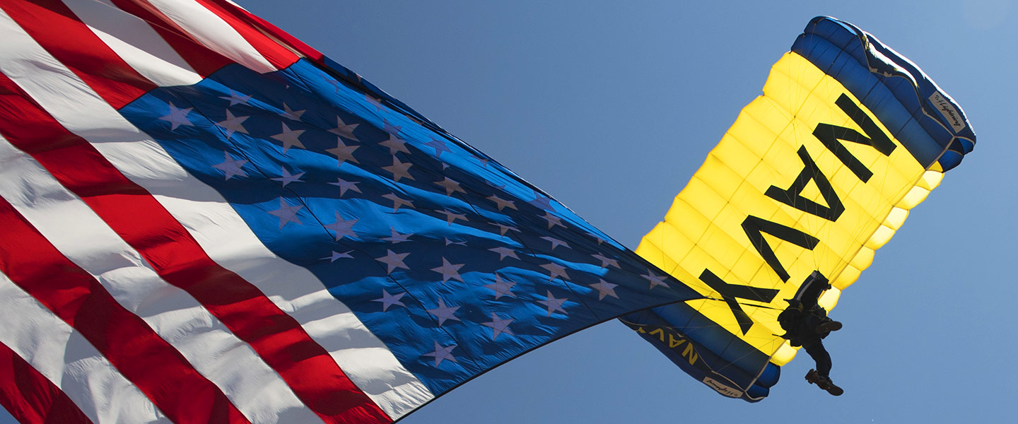 U.S. Navy Leap Frogs parachuter dives above with American flag.