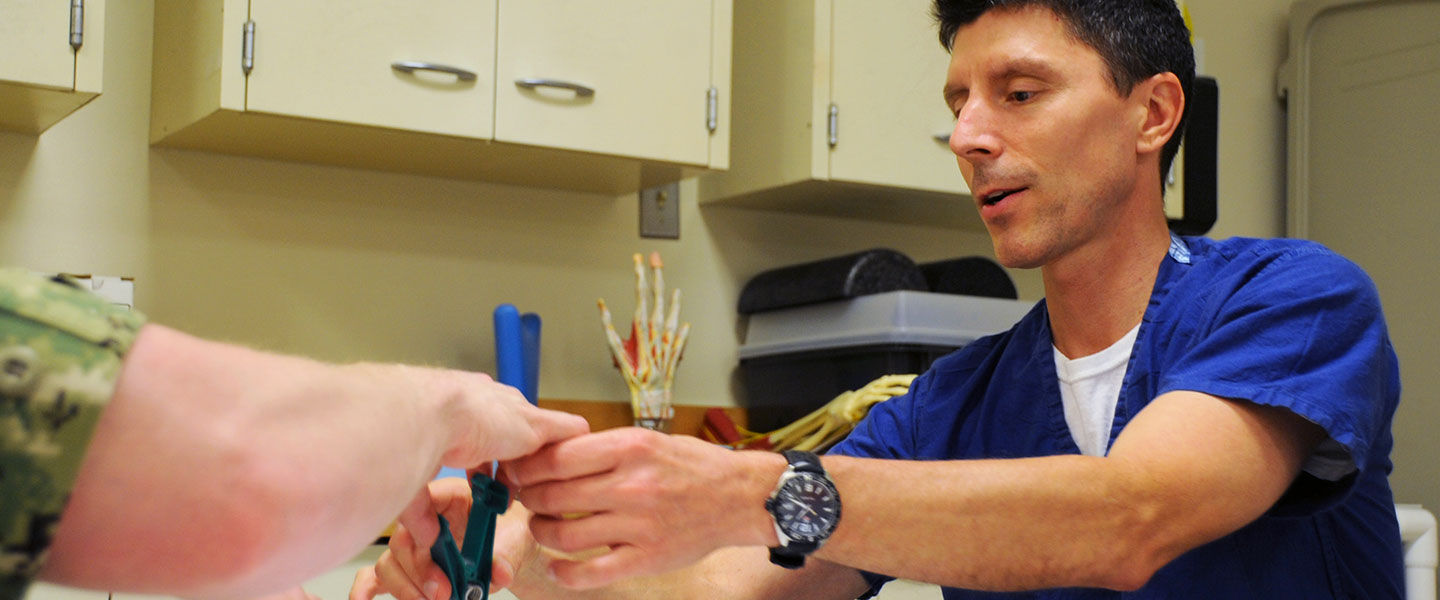 A United States Navy Occupational Therapist uses a therapy tool to test a patient's finger grip and dexterity.