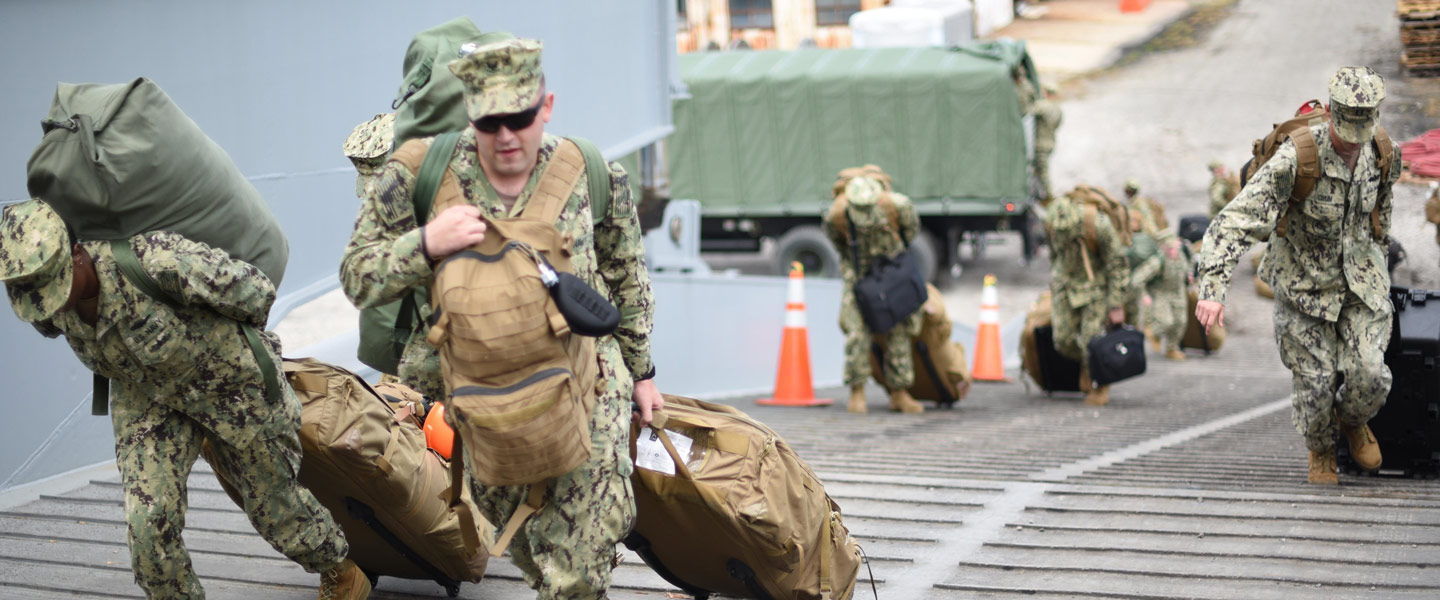 United States Navy Sailors carry their bags onto the ship as they go to sea