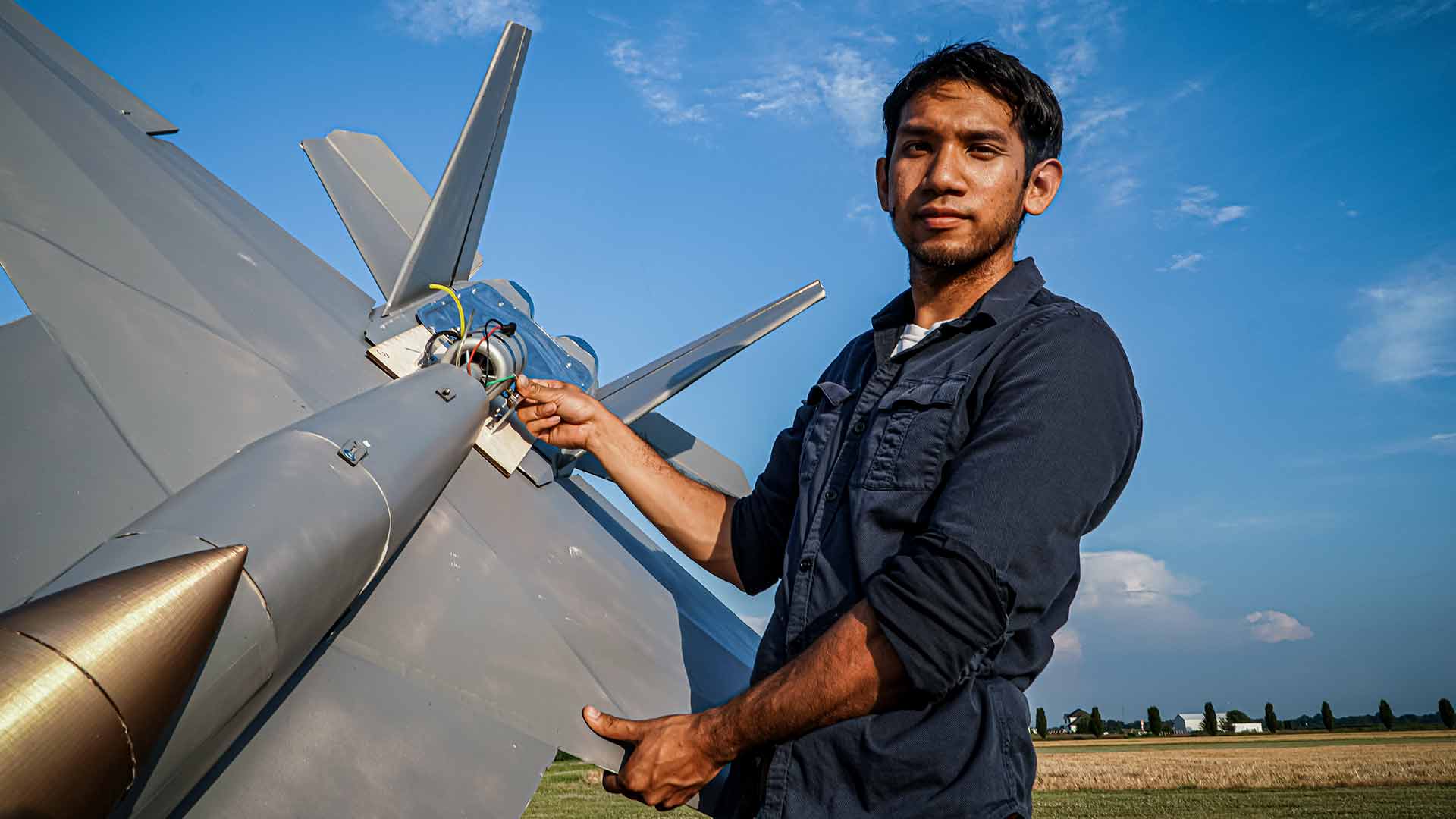 YouTube Creator Peter Sripol stands in an open field holding his large model F-18 as part of the US Navy's Sailor Versus series.