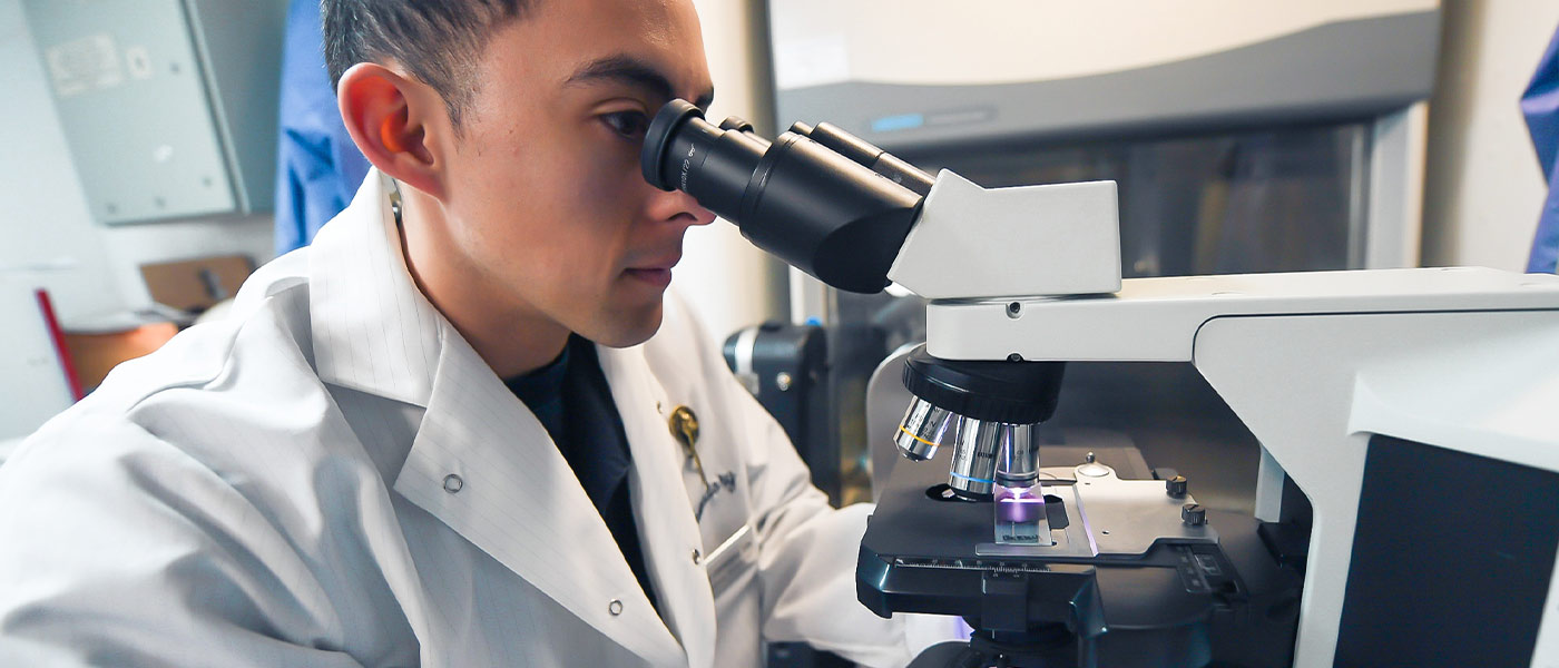 A United States Navy Sailor examines a lab sample under a high-powered microscope.