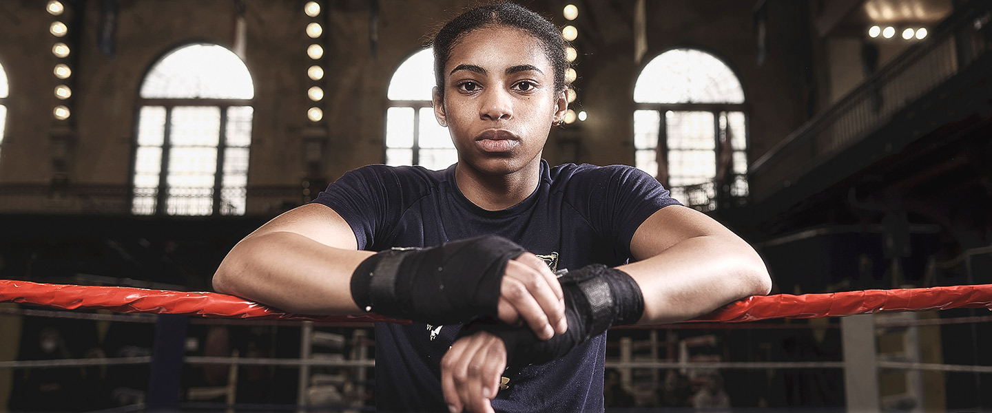 US Naval Academy Midshipman and boxer Kaylah Gillums leans on her forearms on the ropes of a boxing ring.