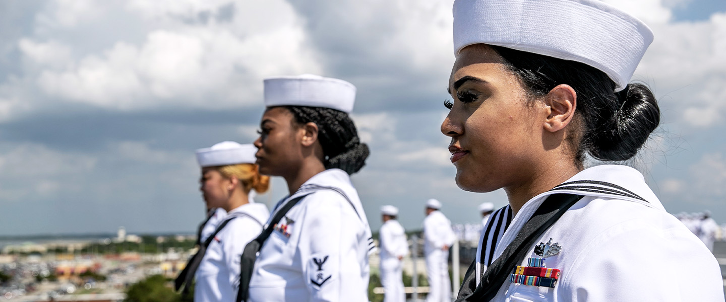 A U.S. Navy Sailor is manning the rails aboard an aircraft carrier.