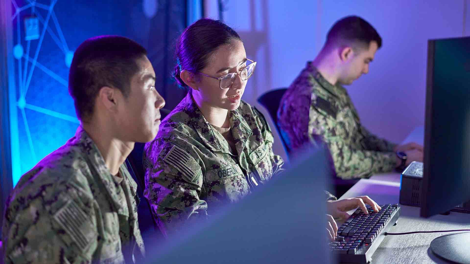 ENS Marie Oberlin works at a desk with other Cyber Warfare Engineers.