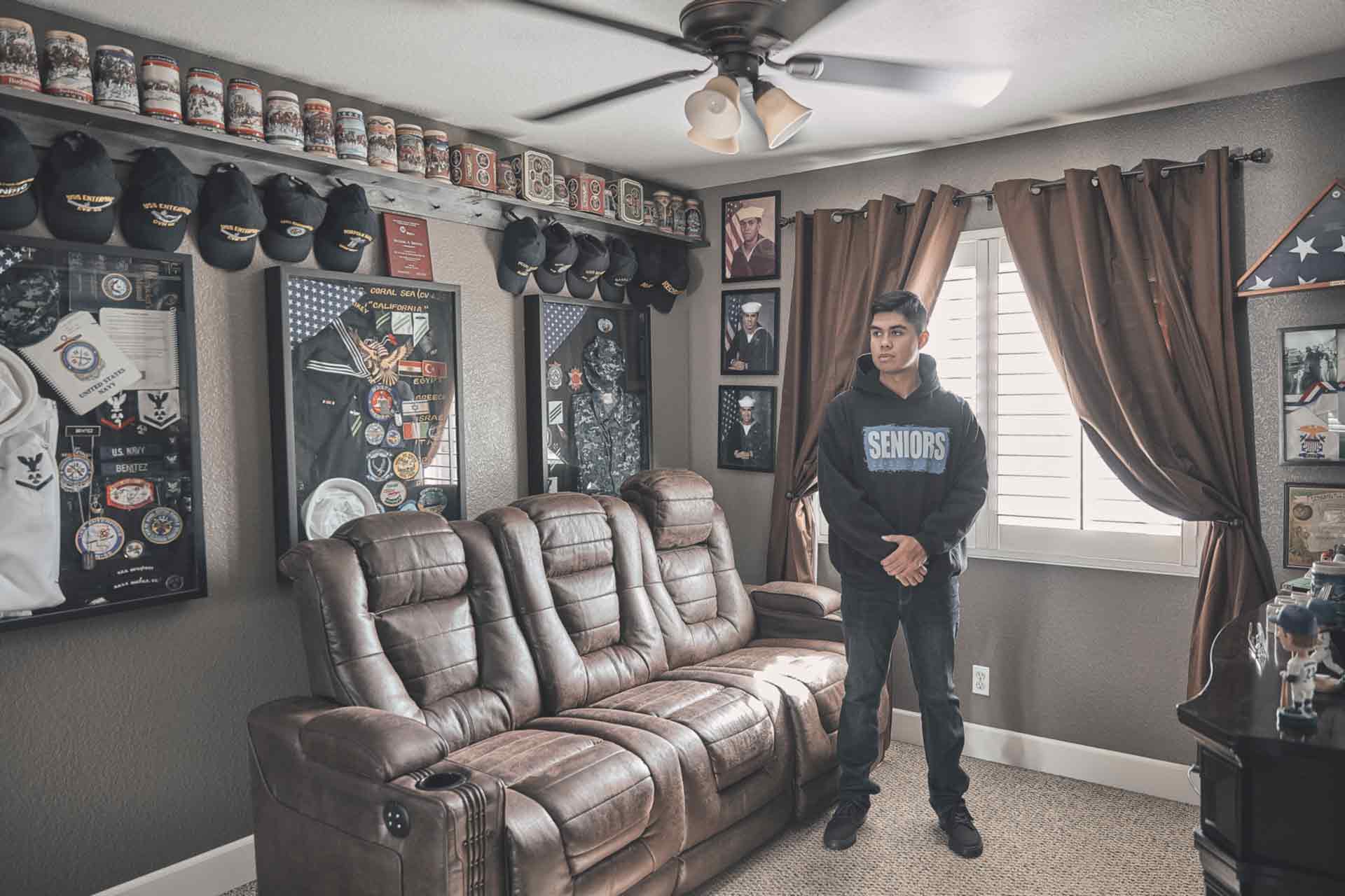 U.S. Navy Sailor Michael Benitez stands in a room at his house surrounded by Navy wall plaques and apparel