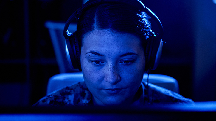 Navy interpreter CTI Myah Riggans wears a headset in a blue-lit navy ship environment while translating Farsi at Naval Support Activity Bahrain