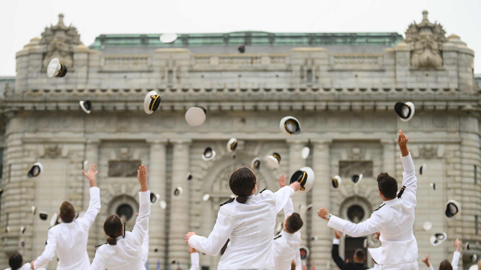 United States Naval Academy graduates toss their caps in celebration in the air.
