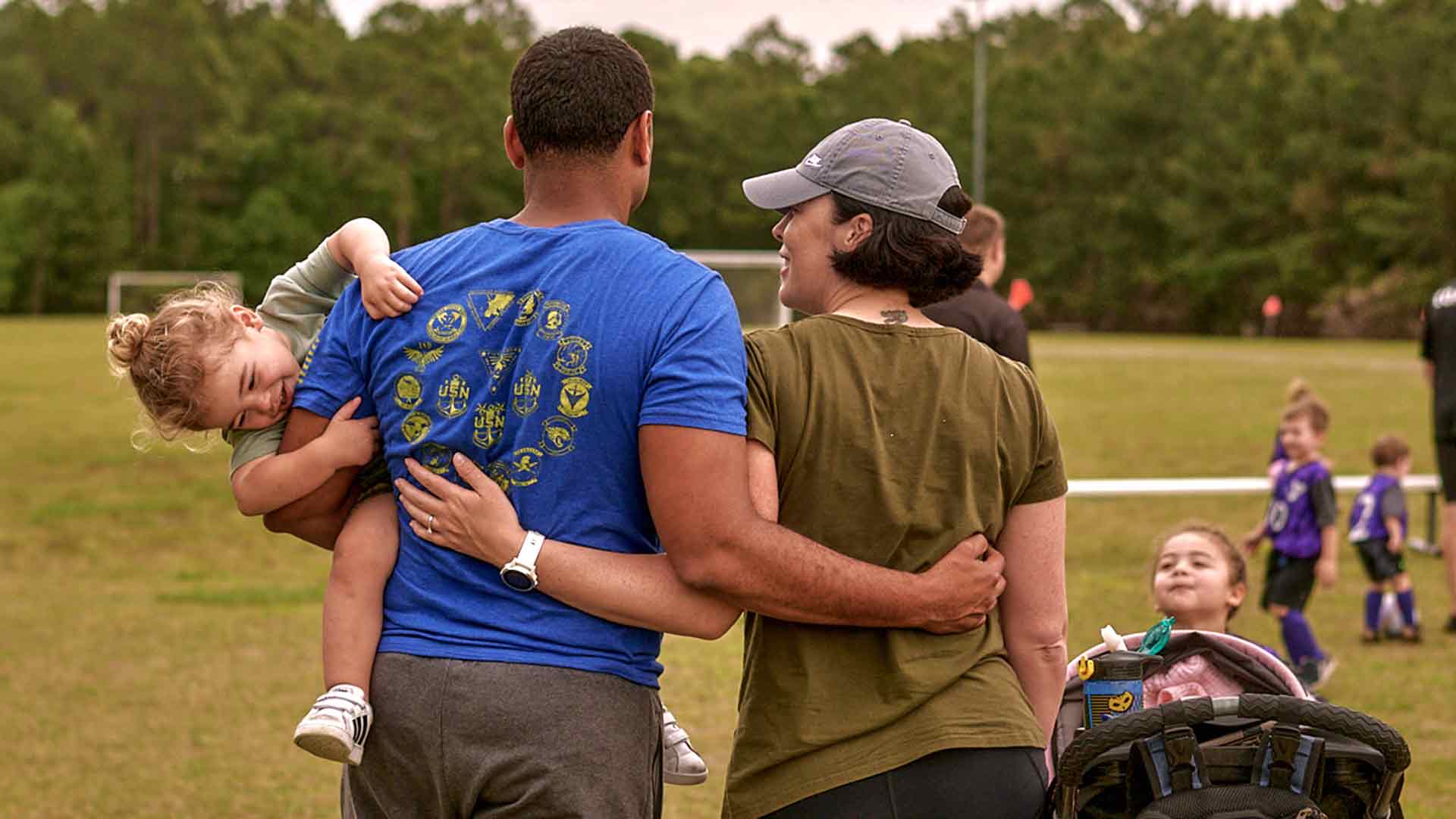 United States Navy Aircrewman Esmelin Villar watches a soccer game with his wife Sarah while holding his child.